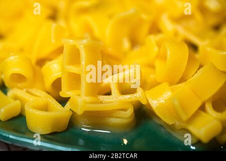 Makkaroni-Alphabet-Buchstaben auf einer grünen Platte. Hartweizenpasta für Kindertisch. Nudeldiät Konzept Stockfoto