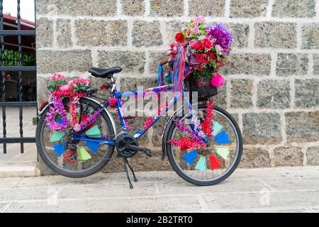 Echtes Fahrrad mit Blumen aus Kunststoff und Stoff, mit einer Wand aus Stein verziert Stockfoto