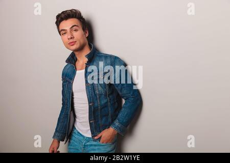 Junger Casual man in Jeans-Jacke an der grauen Wand angelehnt Stockfoto