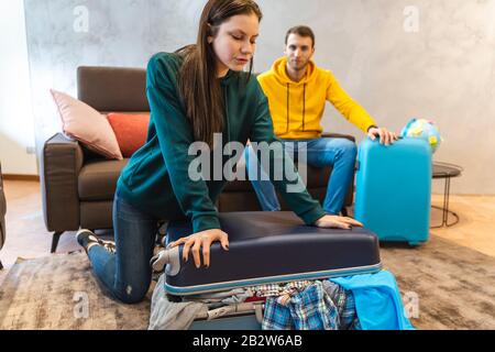 Das junge Paar bereitet die Koffer für die nächste Reise im Wohnzimmer zu Hause vor, Ferien rund um den Globus Stockfoto