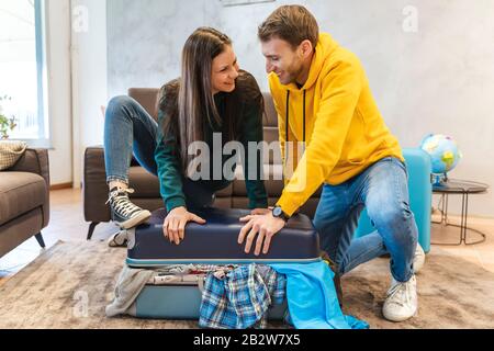 Das junge Paar bereitet die Koffer für die nächste Reise im Wohnzimmer zu Hause vor, Ferien rund um den Globus Stockfoto