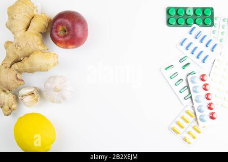 Zitrone, Ingwer, eine Kapelle und Äpfel gegen bunte Tabletten. Das Konzept der Wahl einer gesunden Ernährung im Gegensatz zur Einnahme von Medikamenten Stockfoto