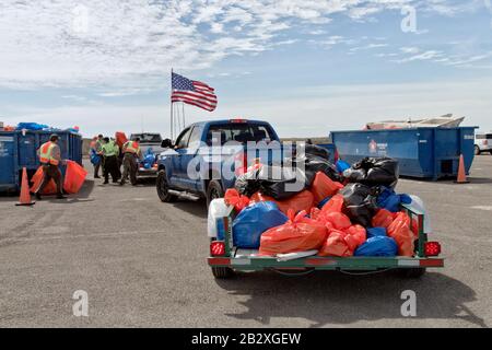 Anhänger, die mit marinen Trümmern und Küstenablagerungen beladen sind, die von Freiwilligen gesammelt wurden, Parkpersonal und Freiwillige, die in Mülltonnen einlagern. Amerikanische Flagge. Stockfoto