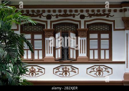 Singapur-Ladenhaus mit braunen und weißen Holzläden und verzierten Steinmetzarbeiten im historischen Geylang in der Außenansicht Stockfoto