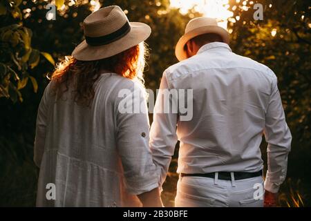 Rückansicht Porträt einer plump kaukasischen Dame mit roten Haaren, die mit ihrem Liebhaber in einem Park mit Hüten und während der Kleidung spazieren geht Stockfoto