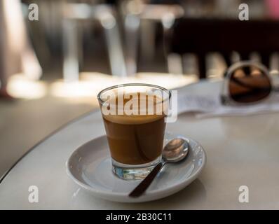 Expresso-Kaffee in kleinem Glas mit Löffel auf weißem Tisch im Restaurant Stockfoto