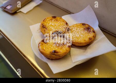 Das portugiesische Ei tarkt Pasteis de nata auf einem mit Puderzucker überzogenen Tresen Stockfoto