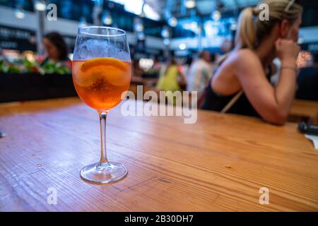 Orangefarbenes Cocktail aus Weinglas, das im Restaurant mit einer Frau im Rücken auf dem Tisch sitzt Stockfoto