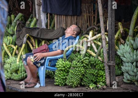 Yangon, Myanmar - Januar 2020: Ein Händler schläft, um seinen Stall grüner Bananen auf dem Bananenmarkt in Yangon zu halten Stockfoto