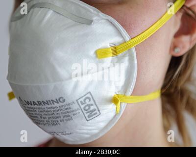 Eine Frau wird mit einem weißen Atemschutzmasken N95 in der Dämmerung in der Nähe gezeigt, das tagsüber vor einem weißen Hintergrund aufgestellt wurde. Stockfoto