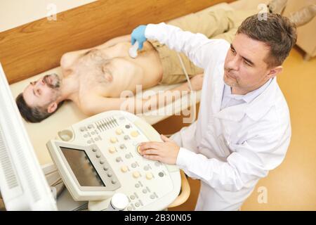 Über der Ansicht des konzentrierten Sonografen im Labormantel mit einer Schallkopfsonde am Bauch des Patienten während des Ultraschallverfahrens Stockfoto