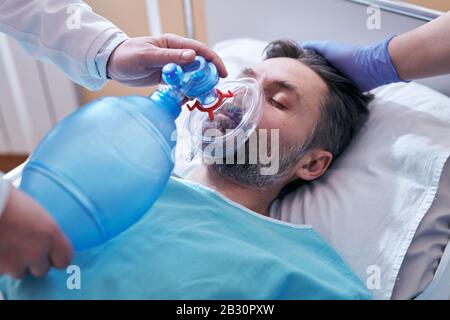 Nahaufnahme eines nicht erkennbaren Arztes, der die Maske des Beutelventils auf das Gesicht eines unbewussten Patienten legt Stockfoto