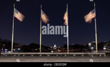 Amerikanische Flaggen winken nachts am Washington Monument. Im Hintergrund ist das US-Kapitolgebäude zu sehen. Stockfoto