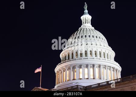 Die US-Kapitol-Kuppel gesehen beleuchtet in der Nacht mit der amerikanischen Flagge vor. Stockfoto
