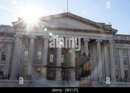 Die Sonne krampft auf das Treasury Building, in dem das US-Finanzministerium ansässig ist. Bronzestatue an Albert Gallatin im Vorderteil. Stockfoto