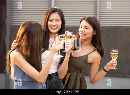 Eine Gruppe junger, wunderschöner asiatischer Frauen, die zusammen mit Freunden ein Glas Wein unterhalten, während sie auf dem Nachtclub auf dem Dach im Freien Tanzparty feiern Stockfoto