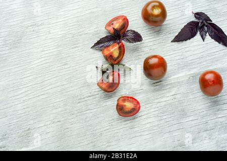 Verschiedene bunte Tomaten und Basilikumblätter über weißem Holzhintergrund. Draufsicht, flacher Lay. Kreatives Layout. Stockfoto