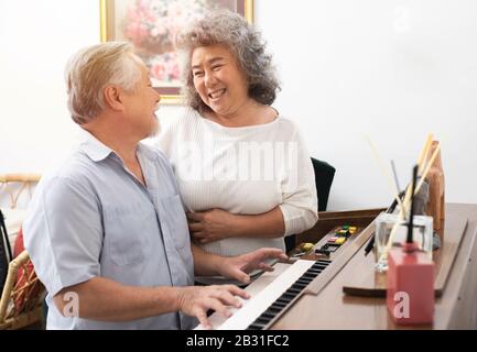 Älterer Mann spielt Klavier im Pflegeheim, das von älterer Frau gehört wird, ältere asiatische Großmutter und Großvater spielen zuhause Klavier Stockfoto