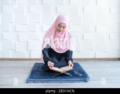 Schöne asiatische weibliche Muslimin in moderner Kurung und Hijab, las quran. Stockfoto