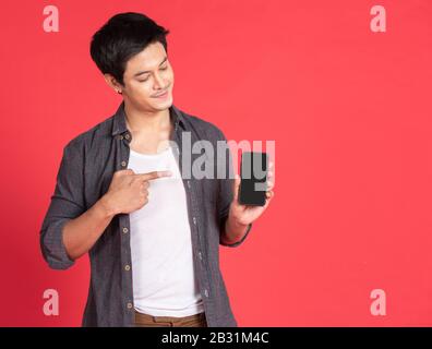 Portrait junger, attraktiver asiatischer Unternehmer oder Student mit Handy, Laptop, Tablet, isoliert auf rotem Hintergrund mit legeren Hemden Stockfoto
