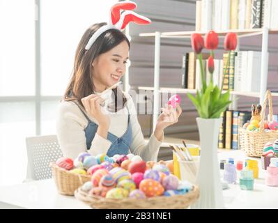 Schöne junge asiatin, die Ostereier mit verzierten Eiern zum Feiern des Ostertags im April mit Kopierraum auf dem Tisch malt. Stockfoto