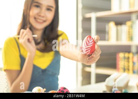 Junge Schönheit fröhliche asiatin mit bunt gebündelten Ohren handgemeltes Gemälde auf farbenfrohem Osterei mit Kunstdesign Pinsel mit dekorativem Stil. Stockfoto