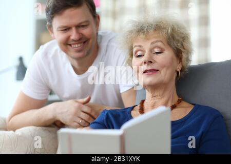 Ältere Dame sitzt Sofa schaut Album mit ihrem Sohn an Stockfoto