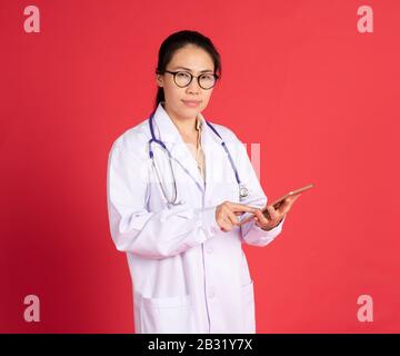 Porträt des lächelnden, schönen asiatischen jungen Frauenarztes mit digitaler Tablette isoliert auf rotem Hintergrund Stockfoto
