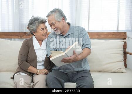 Älteres älteres asiatisches Paar sitzt zu Hause zusammen auf dem Sofa und liest Buch.Mutter Und Großvater verbringen Zeit zusammen im Haus. Stockfoto