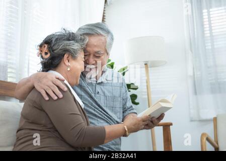 Älteres älteres asiatisches Paar sitzt zu Hause zusammen auf dem Sofa und liest Buch.Mutter Und Großvater verbringen Zeit zusammen im Haus.