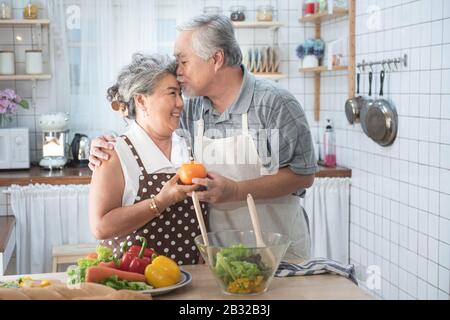 Älteres Paar, das Spaß in der Küche mit gesundem Essen hat - Rentner kochen zu Hause mit Mann und Frau, die das Mittagessen mit Biogemüse zubereiten - H Stockfoto