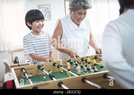 Gruppe der Vielfalt altert Familie, die glücklich zusammen Fußball-Tischspiel spielt. Großmutter spielt zusammen mit ihren Kindern zu Hause Stockfoto