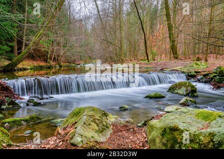 Kleiner Wasserfall ist von Moos und gefallenen Herbst Ahorn Blätter, Langzeitbelichtung umgeben, Feder Szene Stockfoto
