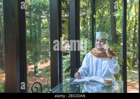 Arabisch-muslimische Unternehmer nutzen Smartphone-Kommunikation und schreiben auf Buch im Café, freiberuflich kein Working Space Lifestyle. Stockfoto