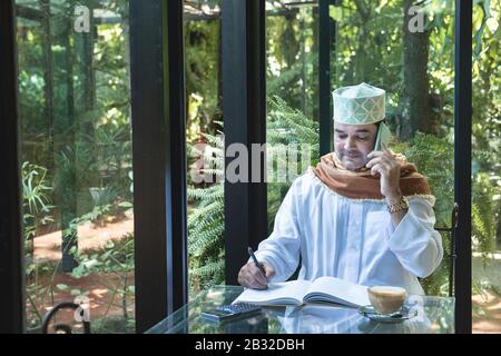 Arabisch-muslimische Unternehmer nutzen Smartphone-Kommunikation und schreiben auf Buch im Café, freiberuflich kein Working Space Lifestyle. Stockfoto