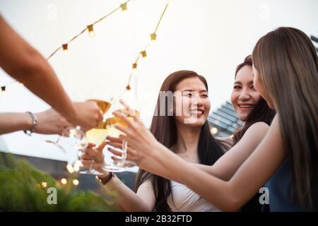 Eine Gruppe asiatischer Vielgeschlechtler hält zusammen mit Freunden ein Glas Wein zusammen und feiert auf dem Nachtclub auf dem Dach im Freien, Freizeitangebot Stockfoto