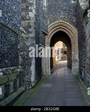 6 Norwich, Norfolk, Großbritannien - 01. März 2020. Dunkle und schmale mittelalterliche Gasse mit Feuersteinwänden an beiden Seiten und einem Architekturbogen am Ende Stockfoto