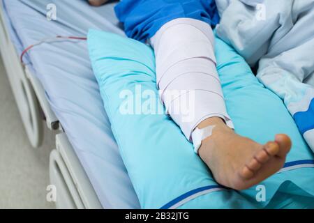 Ältere oder ältere Patienten in Asien, die mit einer Kniestrebe mit Bandkomprimierung liegen, unterstützen Verletzungen im Bett im Krankenhaus der Pflegeanstalt. Stockfoto