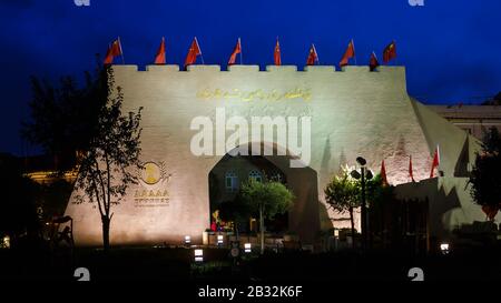 Stadttor zur Kaschgar-Altstadt in der Nacht. Unter dunklem, blauem Himmel. Chinesische Flaggen sind auf dem beleuchteten Tor (Chinese National Holiday) angebracht. Stockfoto