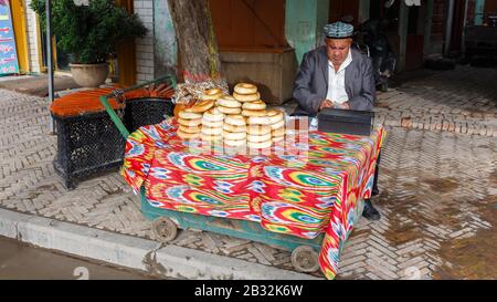 Uyghur man verkauft Girde Naan/Nan auf einem Markt in den Straßen von Kashgar. Traditionelle lokale Küche, die für westliche Augen ähnlich aussieht wie Bagels. Stockfoto