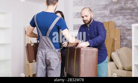 Mann vom Lieferservice, der mit Koffern des jungen Paares in ihre neue Immobilie kommt. Ein Paar zieht in eine neue Wohnung. Stockfoto