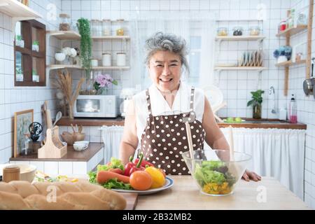 Portrait der älteren, glücklichen asiatischen Großmutter, die in der Küche kochte, alte Frauen bereiten Abendessen im Hobbystil vor. Stockfoto