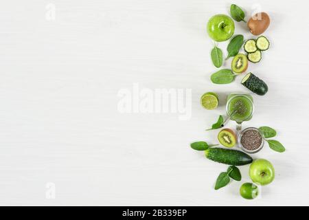 Verschiedene grüne Obst- und Gemüsesorten mit Masonbecher aus Smoothie mit chia-Samen auf weißem Holztisch Draufsicht. Entgiftungsdiät. Gesundes Esskonzept. Stockfoto