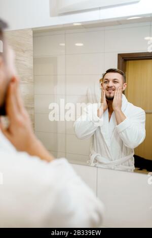 Mann reibt Aftershave über sein Gesicht, Morgenhygiene Stockfoto