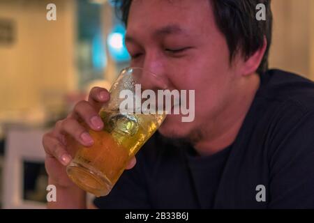 Closeup Asiatischen jungen Mann im Glück Aktion und trinken Bier im Pub und Restaurant mit schwachem Licht Platz, entspannen Sie sich und trinken Konzept Stockfoto