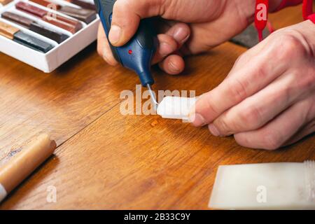 Der Meister schließt den Kratzer ab, die Wiederherstellung von Laminatparkett und Holzmöbel aus der Nähe. Stockfoto