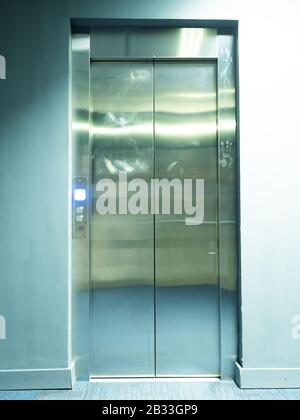Blick auf die metallglänzenden Aufzugtüren mit brennendem, hellen Knopf in der Nähe Stockfoto
