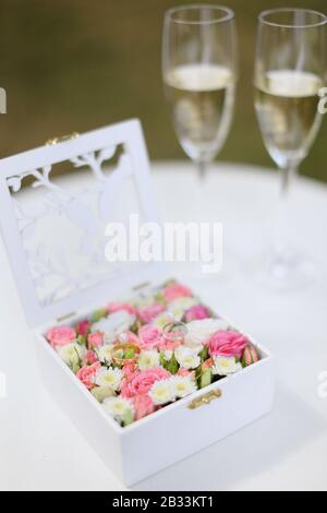 Zwei goldene Ringe in Blumenkiste in der Nähe von Weingläsern mit Champagner. Stockfoto