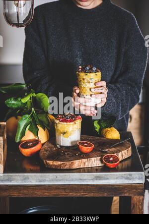 Frau, die ein Glas Müsli mit Mango-Smoothie, Granola und Beeren hält Stockfoto