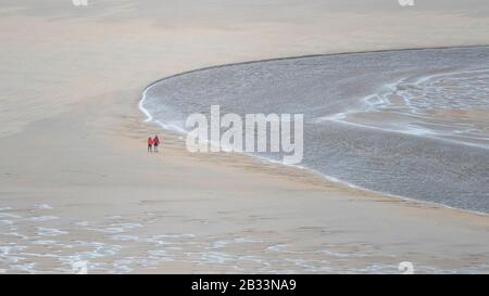 Ein Panoramabild von Wanderern, die bei Ebbe über den Strand von Crantock spazieren, während der Fluss Gannel in Newquay in Cornwal zum Meer fließt Stockfoto